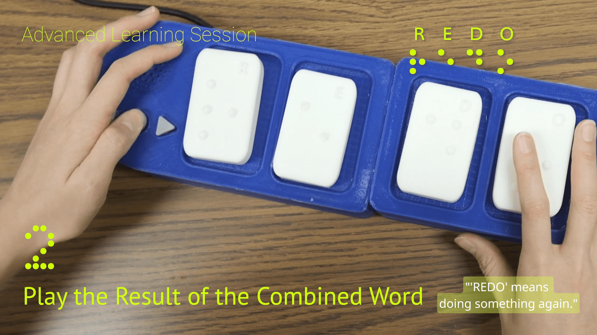 Two boards connected to spell REDO, left hand on the button cluster while the right hand rests on the blocks