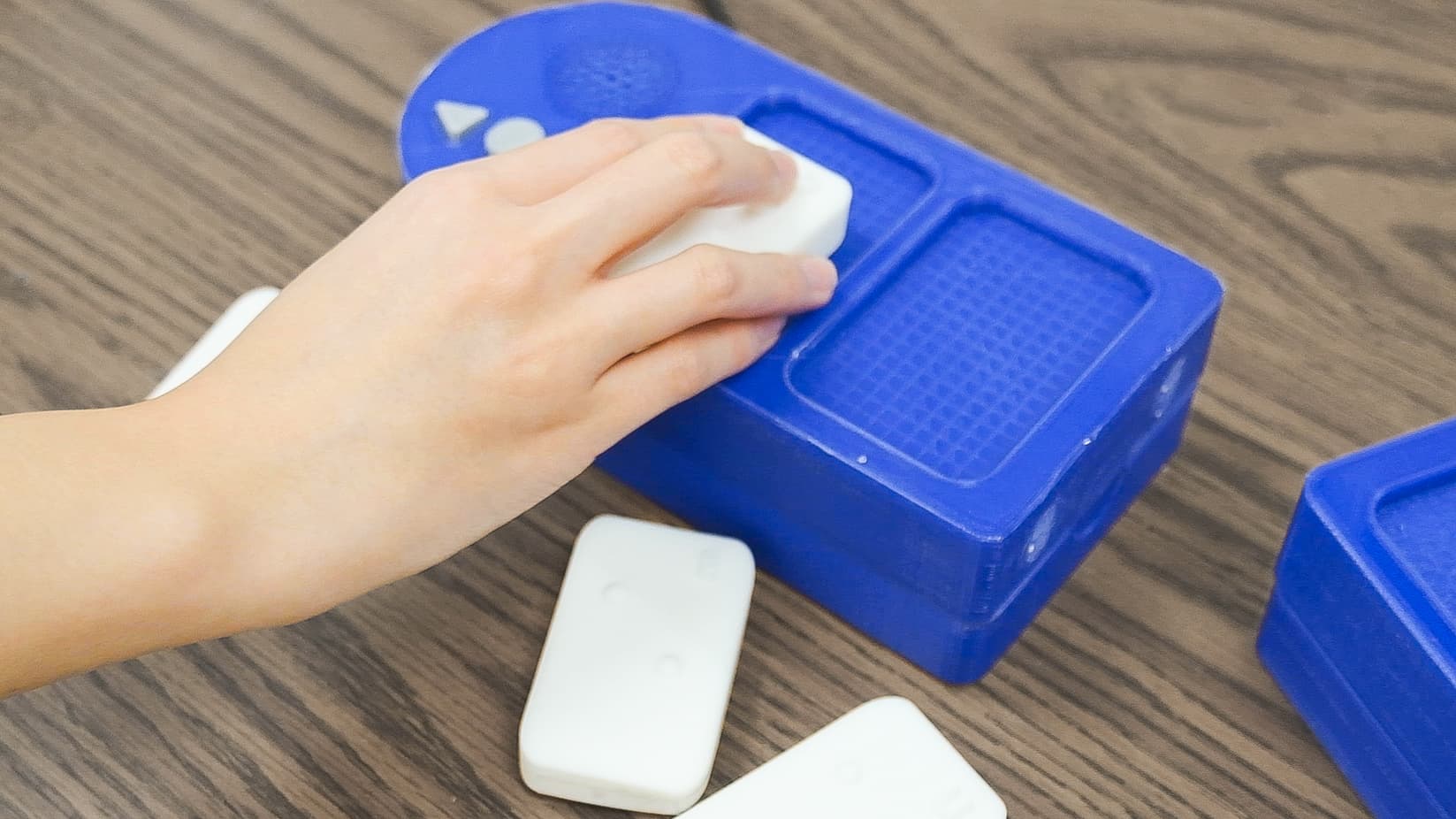 A hand gripping a letter block above the board's textured well